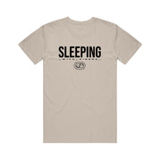 A beige Sleeping With Sirens T-shirt features large black "SLEEPING" above smaller "WITH SIRENS" text and a small pig face graphic—perfect for fans seeking unique band merch.