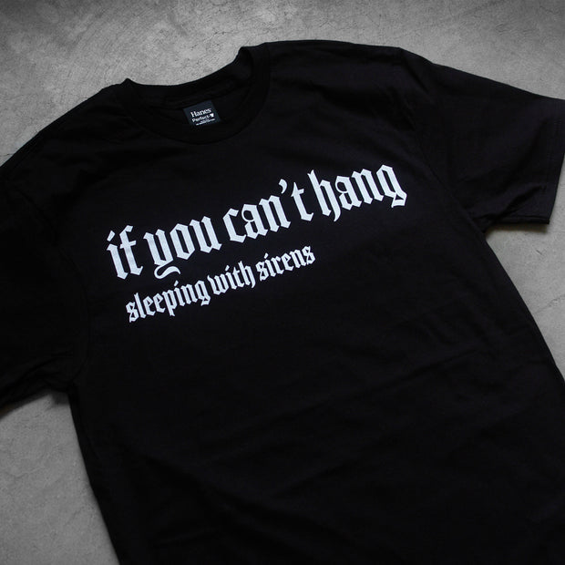 close up, angled image of the front of a black tee shirt laid flat on a concrete floor. front of the tee has a center chest print in white that says if you can't hang. below that says sleeping with sirens.
