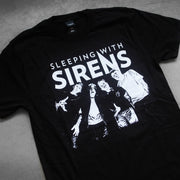 close up, angled image of the front of a black tee shirt laid flat on a concrete floor. tee has a body print in white of a threshold image of the band. above the picture says sleeping with sirens